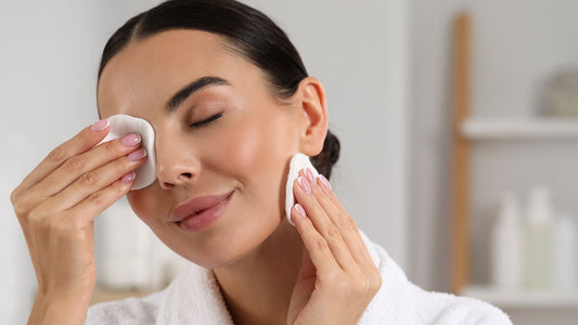 femme aux cheveux bruns avec un chignon qui se démaquille à l'aide de coton