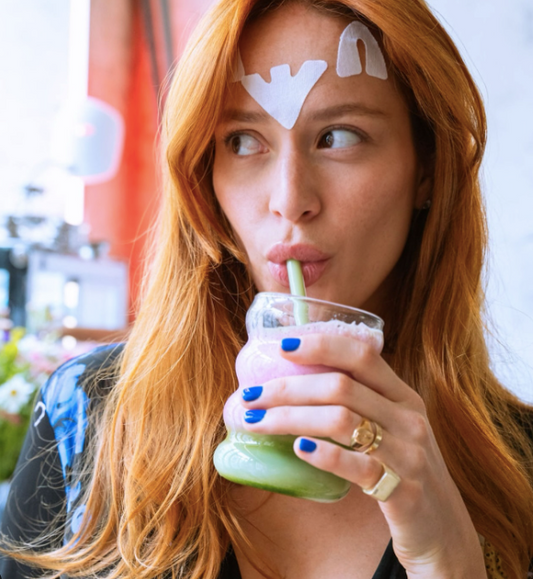 femme rousse avec patch sur le visage qui boit une boisson au collagène de couleur verte