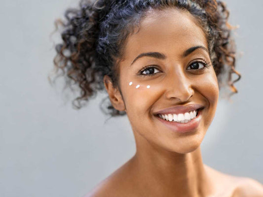 femme de couleur metisse qui sourit avec de la crème sur le contour des yeux